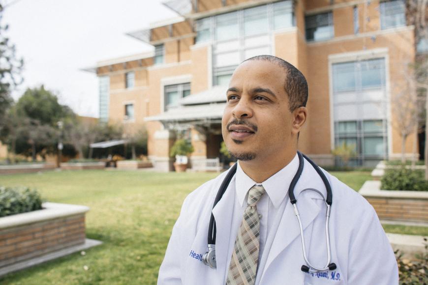 Image of a UC physician in white coat outside near a UC medical facility