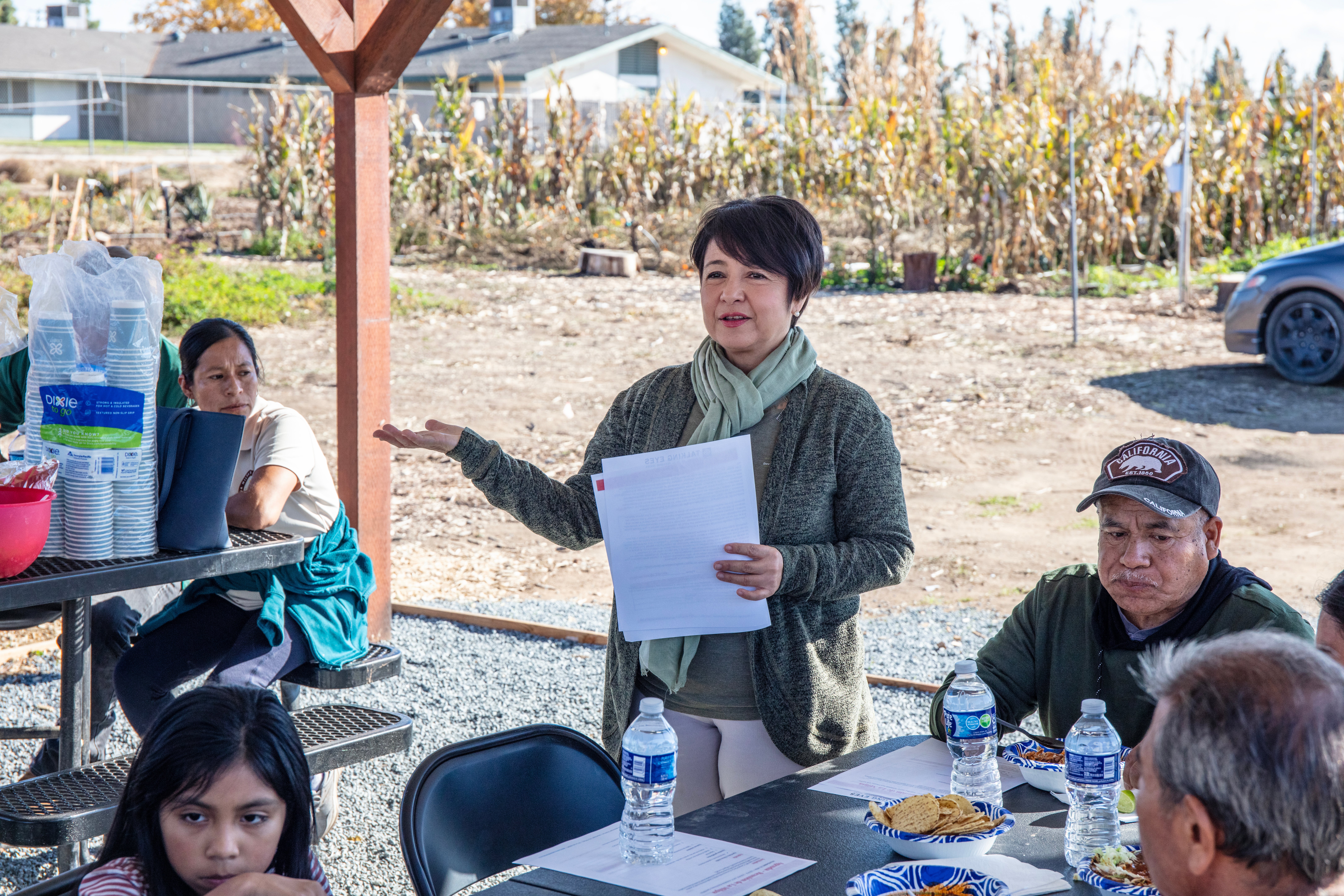A woman speaks outside next to people eating at picnic tables as part of Expanding Occupational and Environmental Medicine Training in Rural Agricultural California, a Grow Grants awarded program