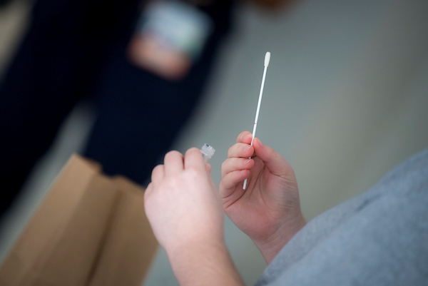Photo of person holding COVID-19 test nasal swab and tube. Credit: Erik Jepsen/UC San Diego