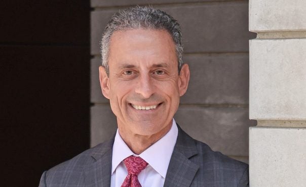Michael J. Stamos, MD, standing near wall in grey suit with red tie