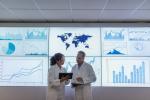 two researchers in white coats standing in front screens presenting data