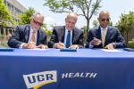 image of three men signing documents sitting on a table that reads UCR Health