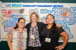 image of three women smiling in front of a poster that says community engagement with words underneath