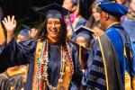 Woman in graduation robe smiling and waving to crowd as she walks across stage