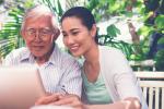 Older man sits next to daughter outdoors while both look at laptop screen in front of them