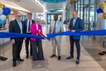 5 hospital leaders stand inside new center each holding part of a blue ribbon while center woman uses large scissors to cut it