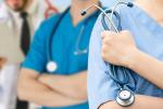 Cropped photo of torsos of three medical professionals with stethoscopes; two are wearing blue scrubs, one has a white lab coat