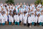 Large group of clinicians in white coat stand side-by-side to pose for camera