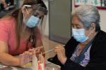 woman wearing mask and face shield helps older woman wearing mask paint a ceramic pumpkin