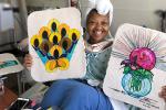 Woman with towel on her head sitting in hospital bed holding two paintings