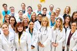 A team of clinicians wearing scrubs and white coats stand side-by-side and smile at the camera