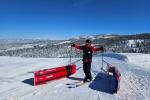 Man in red ski attire raising his hands high with tobaggans in the foreground. 
