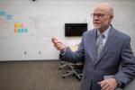 Bill Randall stands in classroom in front of whiteboard gesturing to the side