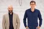 David Brandman and Sergey Stavisky are pictured in front of a wall showing wavy lines from a brain graph. 