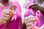 Group of four women with pink shirts holding pink breast cancer ribbons.