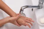person’s hands above sink with water running from faucet over them