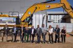 10 people standing in row holding gold shovels with a front loader behind them.