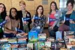 Six women standing behind table covered with books