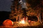 People standing around a campfire at night in the woods next to a tent