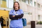 Chelsie Gilbeau wearing blue scrubs standing front of hospital with arms crossed