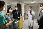 A doctor in white coat stands in hospital hallway conferring with medical students and residents about patients they are seeing 