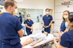 Group wearing blue scrubs surrounding bed with mannequin.