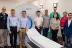 Group of people standing in front of a large PET scanner.