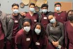 Nine undergraduate students from UC Davis wearing burgundy scrubs and cloth face masks pose for a picture at Imani Clinic