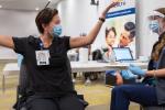 A nurse wearing a surgical mask happily spreads her arms wide after receiving a COVID-19 shot