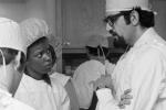 UC Davis physician, right, talks with two reporters. All are wearing white gowns and hats.