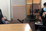 Woman with black mask sitting in chair speaking with a woman wearing a blue mask