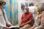 Physician in white lab coat talks with male and female patients wearing masks