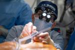 Surgeon operating wearing mask, blue UC Davis head cover and glasses with a light