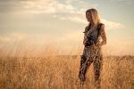 Jackie Anderson holding a camera while standing in a field and looking out at the horizon