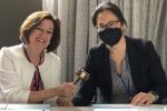 Two women sitting at a table share holding a brown wooden gavel. 