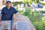 Man with dark skin wearing a blue hat leaning his left arm on a large rock with writing on it.