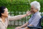 A caretaker smiles at a happy-looking elderly woman in a wheelchair
