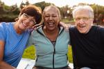 Three older adults sitting on grass next to each other smiling at camera