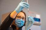 Woman wearing a blue mask drawing liquid out of a vile with a syringe