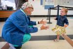 Man in nurse uniform holds arms out and toddler girl with pigtails runs toward him smiling.