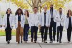 A group of 10 students, most in white coats, stand side by side as they walk in a courtyard at the UC Davis School of Medicine.
