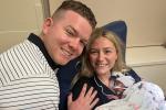 Man puts his hand on woman's shoulder as she holds newborn baby.
