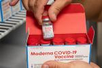 Pair of hands holding Moderna vaccine vile and box.