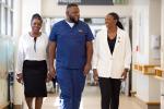 Aron King center, walks in hospital hallway looking at DaJanae Gresham-Ryder on the right, while Calene Roseman stands on Aron’s left looking forward
