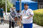 Masked lady with walker walks behind nursing student in scrubs holding paper