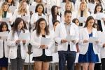 A group of P.A. students wearing white coats stand shoulder-to-shoulder reading their oath