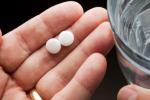 Hand holding two pills and glass of water