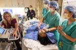 Surgeons use handheld tool on patient lying on table while looking at monitor being staffed by technician