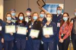 Nurses wearing blue scrubs holding certificates and wearing masks