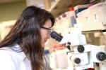Woman wearing white coat and looking into a microscope